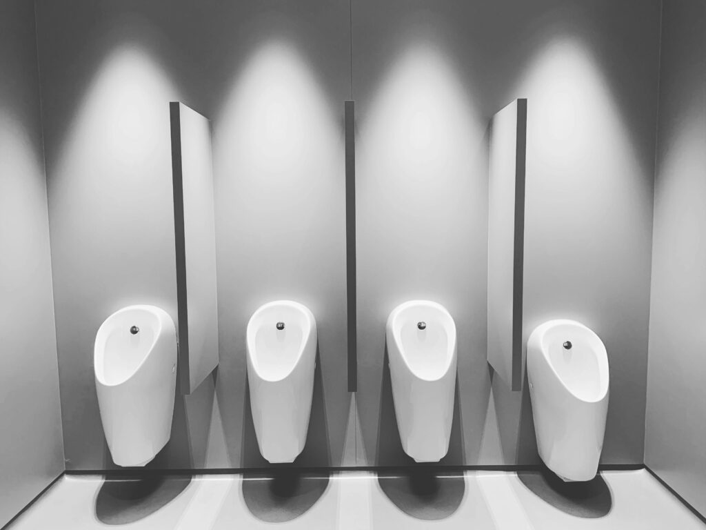 A clean and modern restroom featuring four white urinals and partitions.