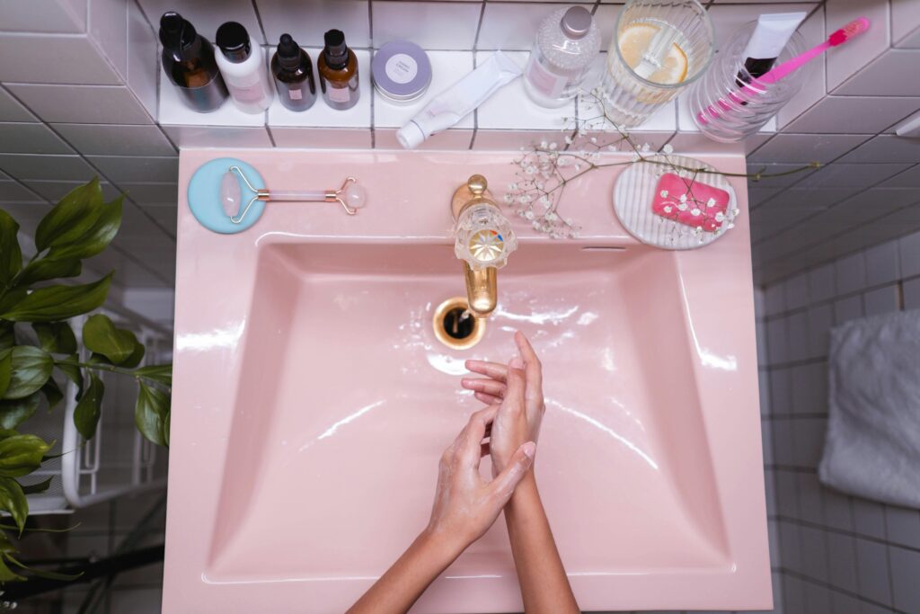 A stylish bathroom setup with skincare products and a person washing hands in a pink sink.